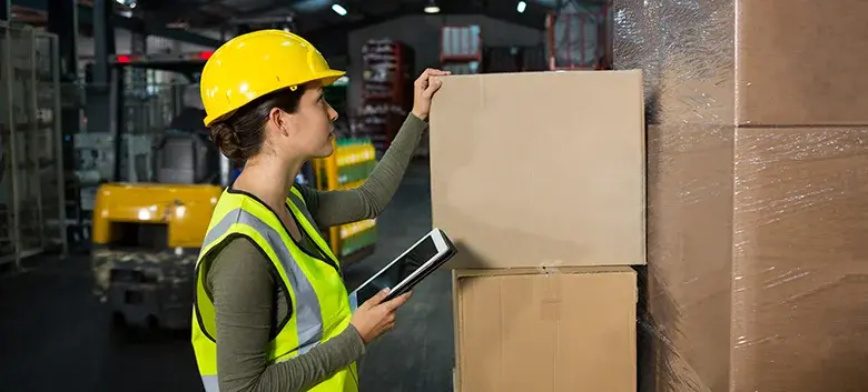 Operaria logística con casco y tableta organizando cajas: Transporte de carga en Bucaramanga y Santander.